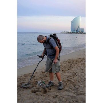 customer seeking silver and gold objects lost coins, on the beach with a metal detector in Barceloneta's beach in Barcelona