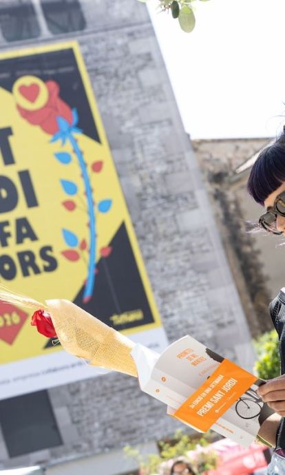 Una dona llegint amb el cartell de Sant Jordi ens fa millors© Àngel Bravo