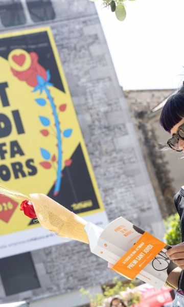 Una dona llegint amb el cartell de Sant Jordi ens fa millors© Àngel Bravo