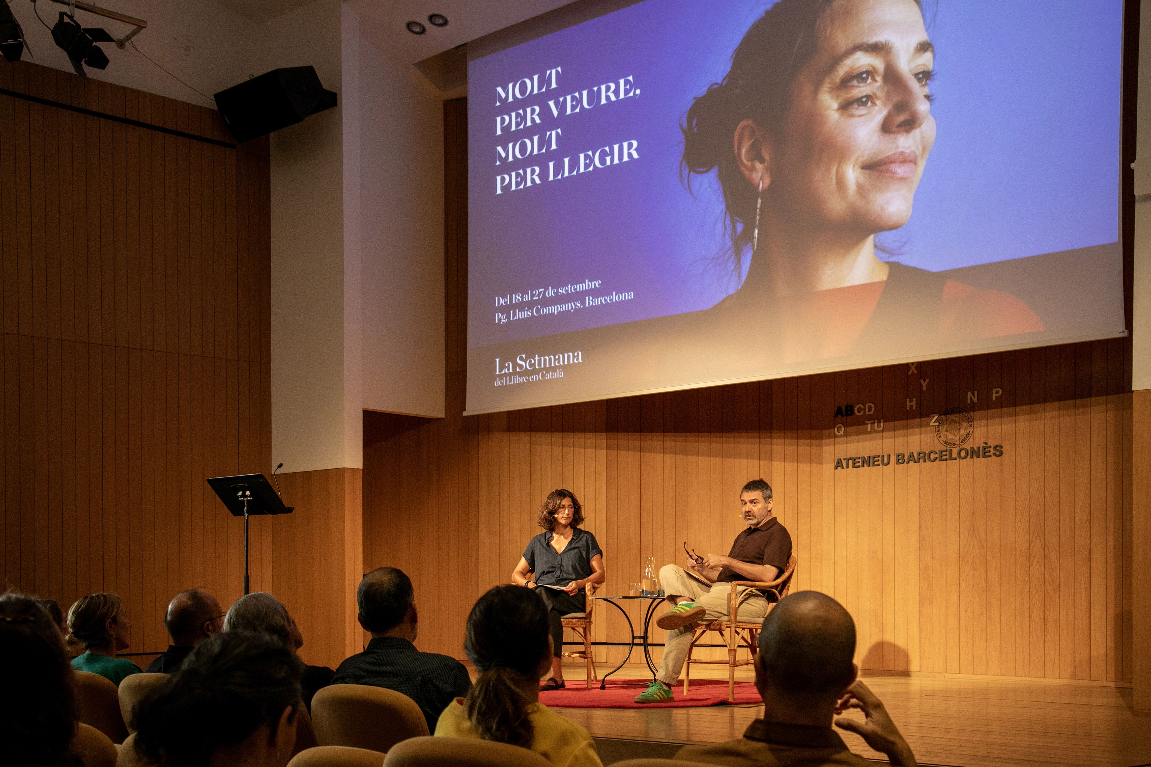 Cristina Domènech, directora de la Setmana, i Oriol Magrinyà, president d'Editors.cat, durant la presentació del programa, amb el cartell de fons. 