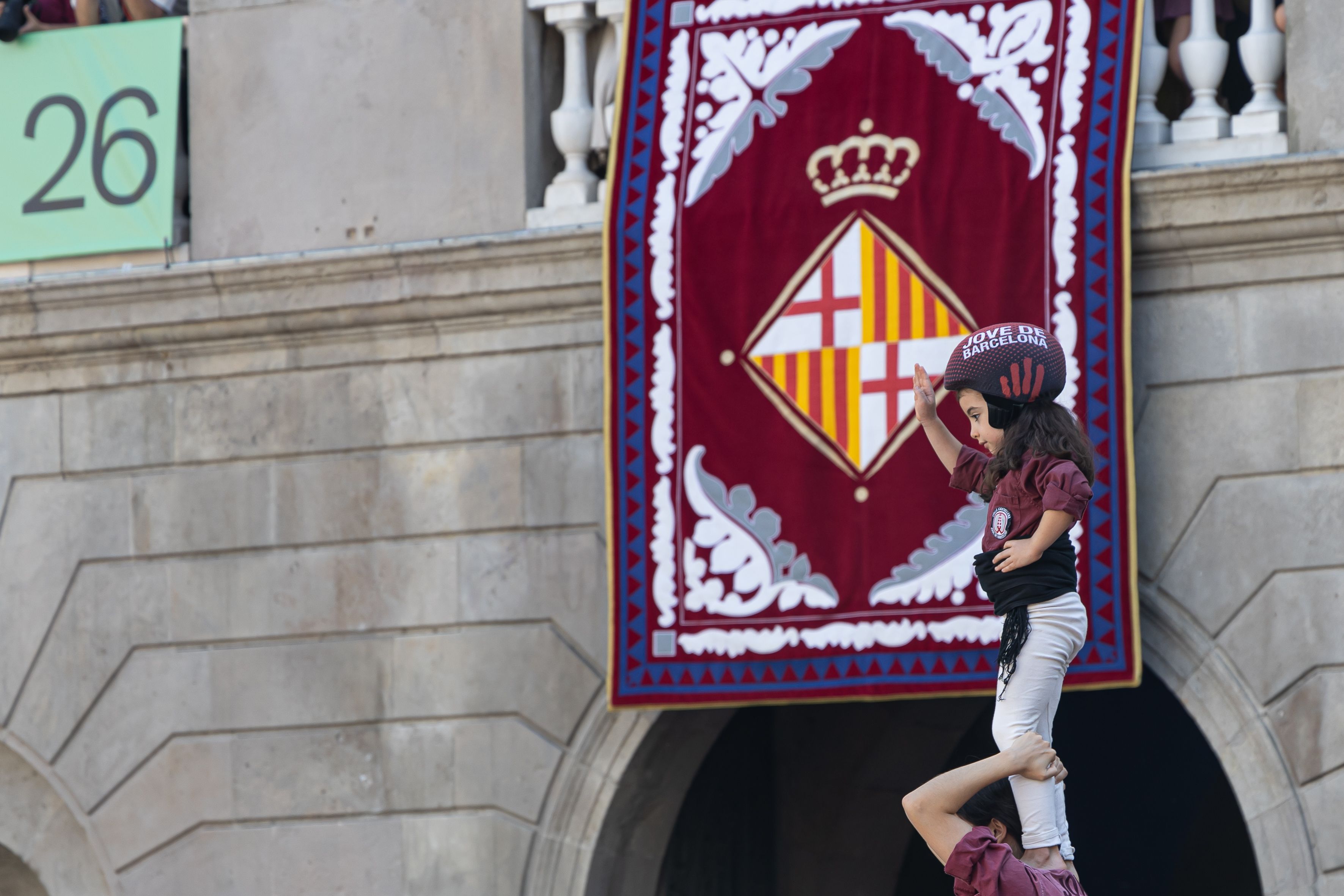 L’anxaneta de la Colla Jove de Barcelona culmina el castell amb el balcó de l’Ajuntament, engalanat amb l’escut de la ciutat, com a teló de fons. © Àngel Bravo