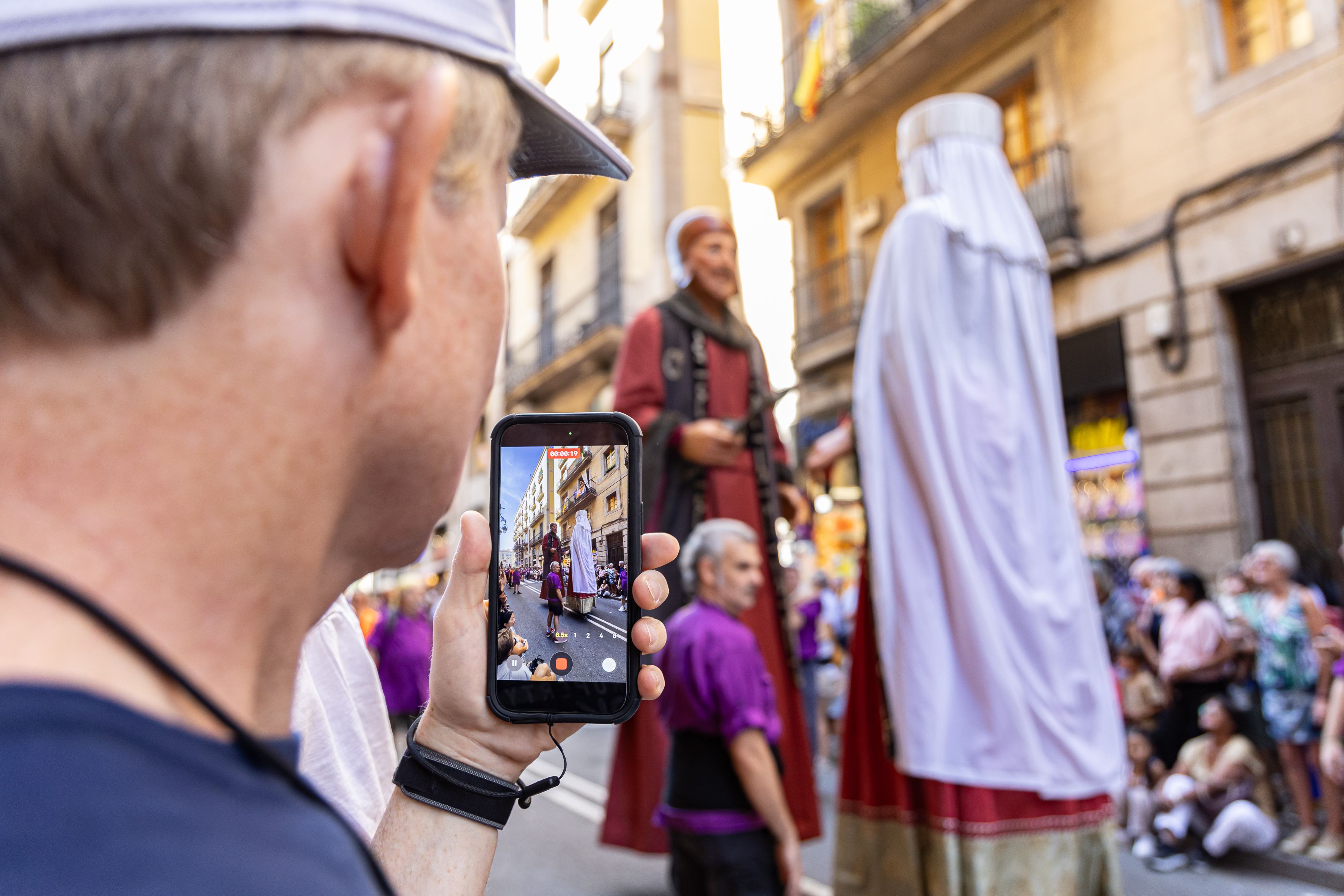 Amb el mòbil en mà, un espectador grava el pas dels Nans i Gegants pels carrers de Barcelona durant la Mercè. © Àngel Bravo